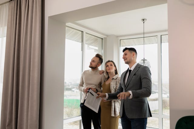 a man in a suit holding a clipboard showing a house to a couple